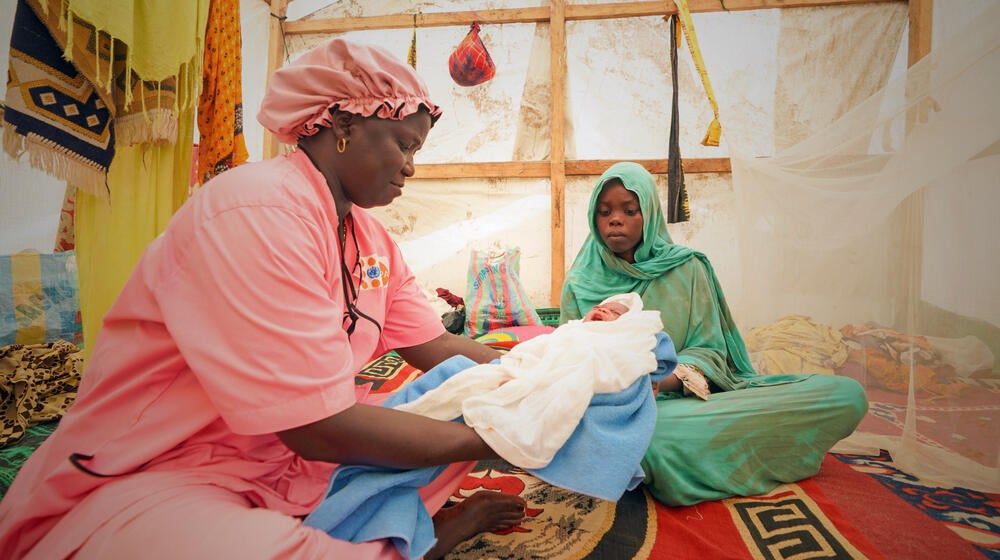 A midwife is holding a new born and is sitting beside the mother.